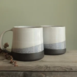 Two minimalist stacked mugs on wood with green wall